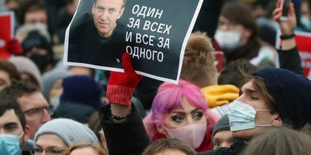A man standing in a large crowd holds an image of Alexei Navalny.